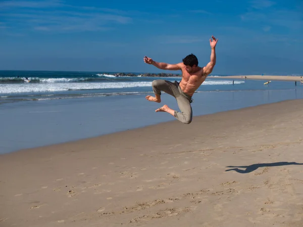 Full length happy barefoot guy jumping in excitement while resting on sandy beach