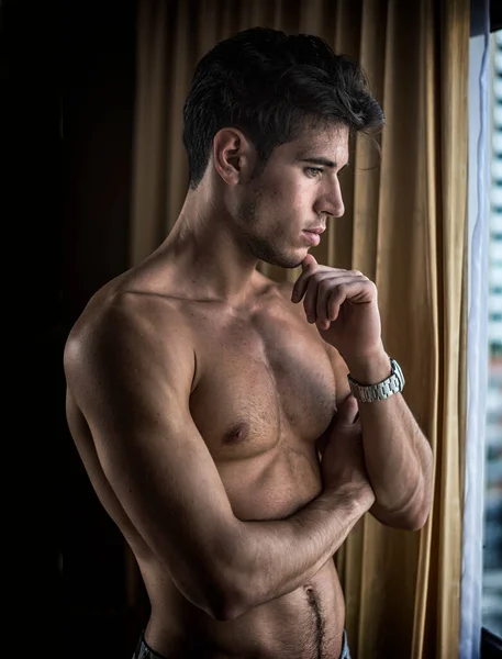 窓のカーテンの横にある彼の寝室で上半身裸で立っているセクシーなハンサムな若い男 — ストック写真