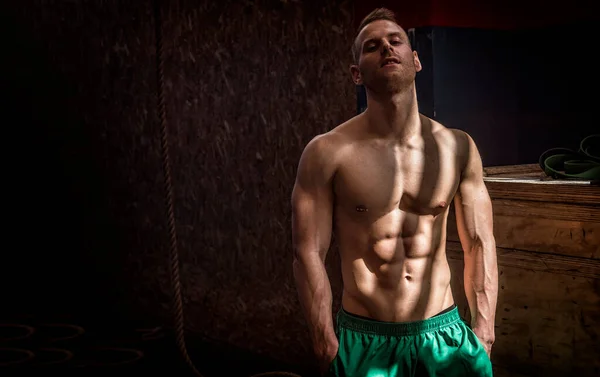 Handsome muscular young man standing in gym during workout, looking at camera