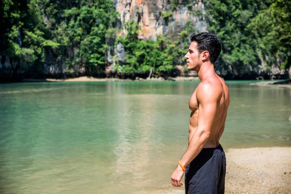 Half body shot of a handsome young man standing on a beach in Phuket Island, Thailand, shirtless wearing boxer shorts, showing muscular fit body