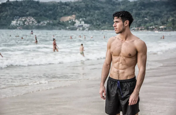 タイのプーケット島のビーチに立っているハンサムな若い男の半分の体のショットは 筋肉フィットボディを示す ボクサーショーツを身に着けている — ストック写真