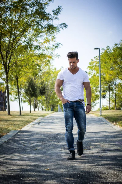 Attractive muscular man in city park in a nice summer day walking. Full length shot