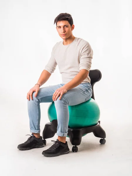 Full body of male sitting on balance ball chair with hands on legs, on white background looking at camera