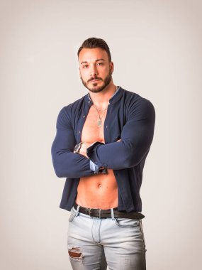 Beyaz tişörtlü, kollarını kavuşturup kameraya bakan, çıplak gövdesi açık, zarif, çekici genç bir adam.