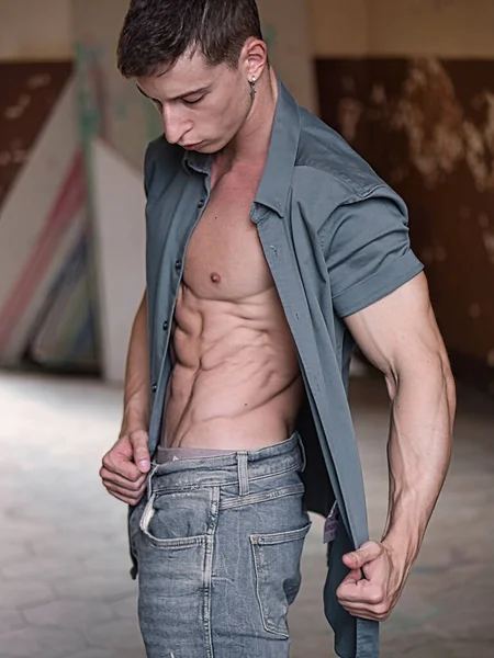 魅力的な若い男のオープニングシャツは 裸の胴にジーンズやシャツを着て 筋肉質の体を表示します — ストック写真