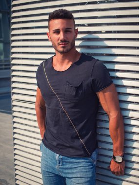 Avrupa 'da şehir merkezinde kot pantolon ve siyah tişört giyen yakışıklı bir genç.