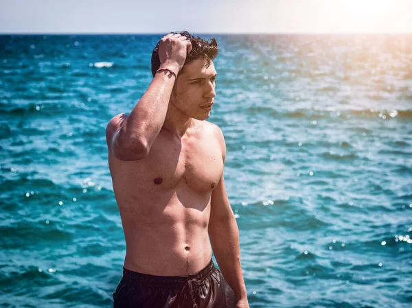 Junger Athletischer Mann Steht Meerwasser Ohne Hemd Und Badeanzug Schaut — Stockfoto