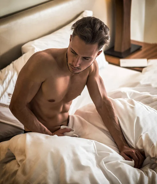 マグやカップを手にコーヒーまたは紅茶が付いているベッドに筋肉のついた体で完全に裸のセクシーな若い男 — ストック写真