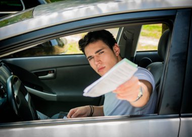 Genç ve çekici bir erkek arabada oturuyor ve elinde belgelerle elini uzatıyor..