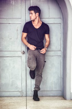 Handsome young man outdoors in front of old house's wood entrance door, looking away to a side clipart