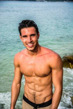 Denizdeki çekici genç adam ıslak saçlarıyla sudan çıkıyor, kameraya bakıp gülümsüyor.