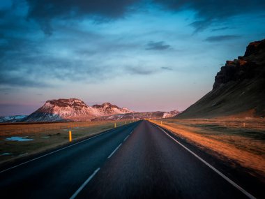 Modern araba İzlanda gezisi sırasında asfalt kırsal yolda muhteşem karlı dağlara doğru gidiyor.