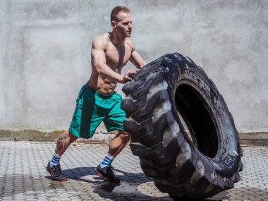 Yakışıklı, kaslı, spor yapan, büyük kamyonet lastiği takla atan genç bir adam.