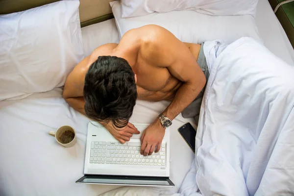 裸の若いです男とともにベッドの上にマッグやカップで手にコーヒーや紅茶 ノートパソコンのコンピュータ画面を見て — ストック写真