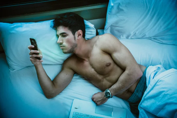 深夜在床上用手机打字 发短信 拨号或阅读网页的英俊年轻人 — 图库照片