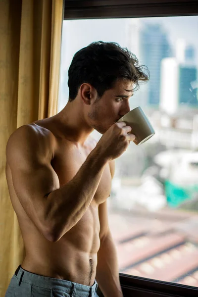 性感英俊的年轻人赤身裸体地站在卧室里 在窗帘旁边喝咖啡或茶 — 图库照片