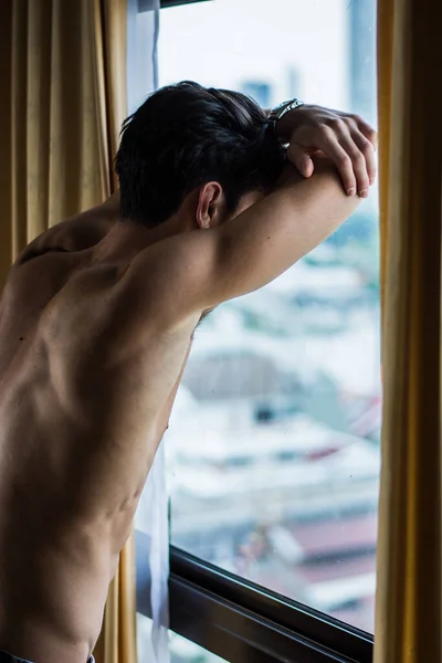 窓のカーテンの横にある彼のベッドルームで恥知らずな立ってセクシーな若い男 外を見る — ストック写真