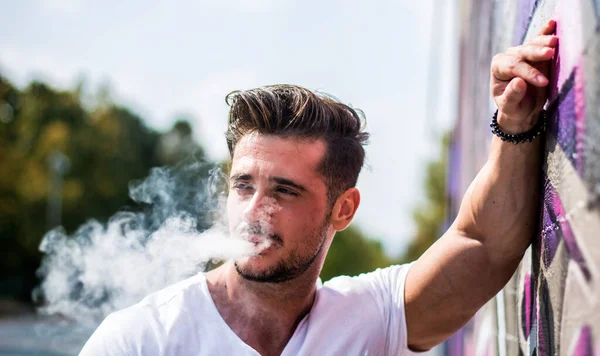 ハンサムな男は 都市の設定で屋外を蒸気タバコを吸う — ストック写真