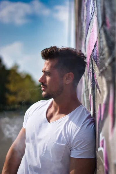 Ελκυστικός Μυώδης Άνδρας Ακουμπά Στον Πολύχρωμο Τοίχο Γκράφιτι Φορώντας Λευκό — Φωτογραφία Αρχείου