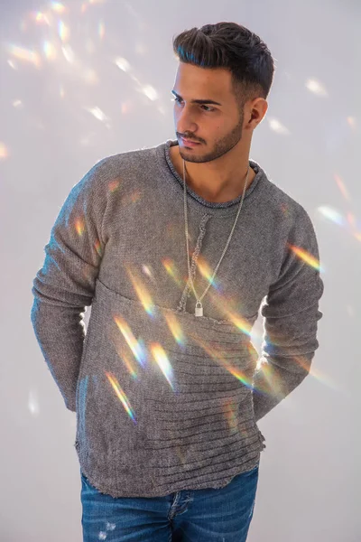 身穿灰色毛衣的英俊的纹身青年男子 站在明亮的背景下 在演播室里拍摄 身上闪烁着微光 — 图库照片