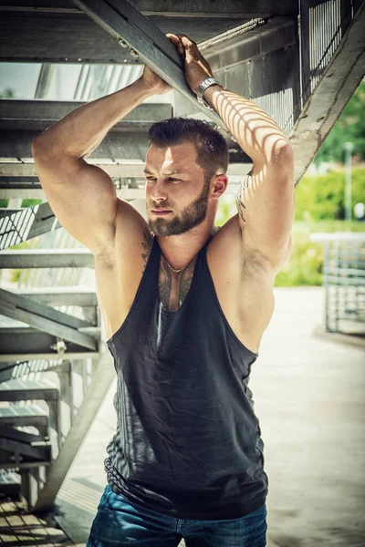 在城市公园的金属楼梯下面 一个英俊的肌肉运动员 白天穿着黑色的背心 — 图库照片