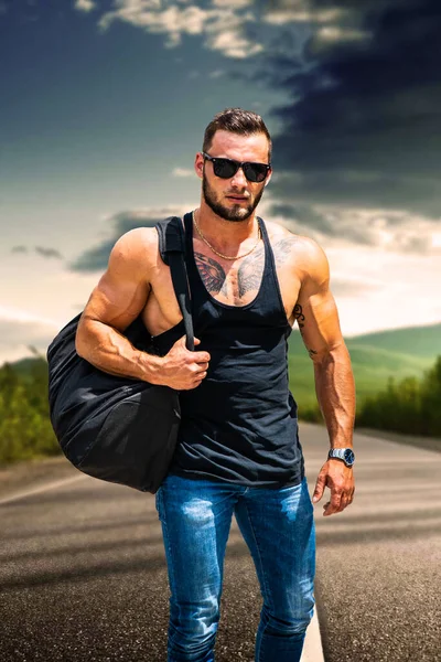 黒いTシャツを着て大きな袋を持って空の道を歩くハンサムな筋肉運動選手 — ストック写真