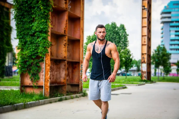 日中に市内公園でランニングやジョギングをしているハンサムな筋肉質の運動選手は 黒のタンクの上を着て — ストック写真