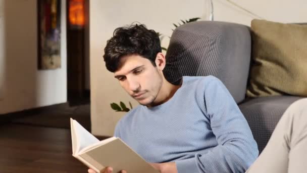 Schöner Junger Mann Liest Hause Seinem Wohnzimmer Buch Und Sitzt — Stockvideo