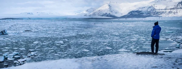 氷の海の近くに立っているアウターウェアの認識できない男性観光客の完全な体のバックビューとアイスランドの雪の山の絵のような風景を賞賛 — ストック写真