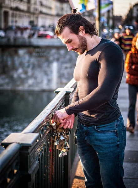 歩道橋の上に立つカジュアルな服を着た髭の男の側面図と金属の手すりに愛のロックを取り付ける — ストック写真