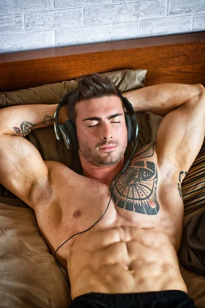 Shirtless muscular sexy male model lying alone on bed in his bedroom, relaxing with eyes closed