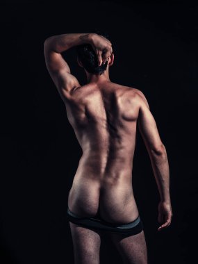 Bir stüdyo ortamında, kaslı bir adam kendine güvenerek iç çamaşırını indirir, ve heykel gibi kalçalarını ortaya çıkarır. Çekim, onun cesur ve kendinden emin duruşunu yakalar ve fiziksel formunu gösterir. Kas gücü