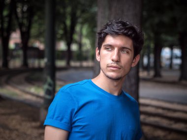 Şehir ortamında mavi polo tişörtlü yakışıklı bir adamın dörtte üçü, başka tarafa bakıyor.