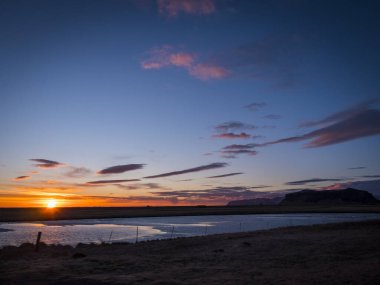 Güneş bir su kütlesinin üzerinde batıyor. İzlanda 'nın sakin bir su kütlesinin üzerinde güzel bir günbatımının fotoğrafı