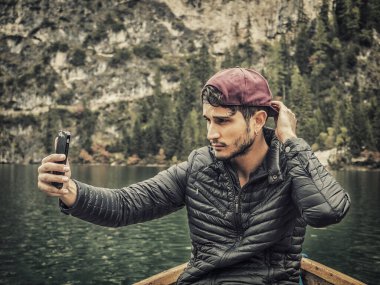 Teknede cep telefonu tutan bir adam. İtalya 'daki Dolomitlerin manzaralı güzelliğinin tadını çıkaran bir adamın fotoğrafı. Bir botta cep telefonunu kullanırken.