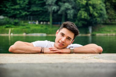 Bir adam kafasını bir su kütlesinin yanındaki kayaya yaslıyor. Kafasını suyun kenarındaki bir kayaya yaslamış bir adamın fotoğrafı.