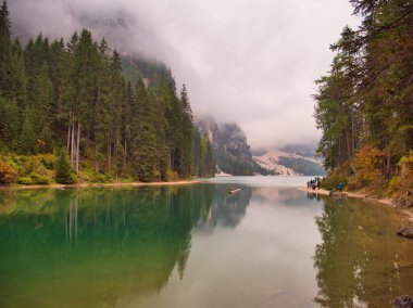 Ağaçlar ve dağlarla çevrili bir su kütlesi. İtalyan Dolomitleri 'ndeki görkemli dağların arasına yerleştirilmiş dingin bir gölün fotoğrafı