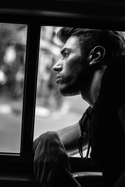 A young attractive man sitting in a car looking out the window, black and white photo
