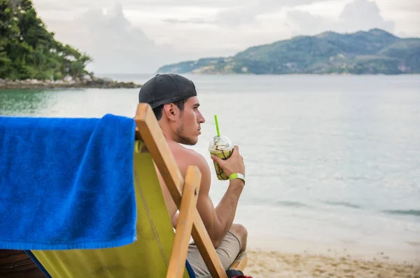 A man sitting on a beach holding a drink. Photo of a man enjoying a refreshing drink while soaking up the sun on the beach