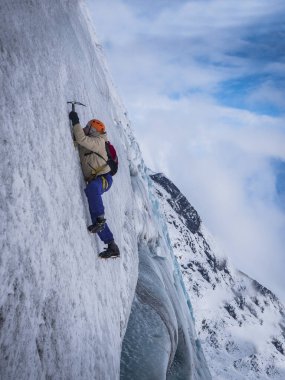 İzlanda 'da bulutlu gökyüzüne karşı dağların buzlu yamacına tırmanan kalın elbiseli bir erkeğin yan görüntüsü