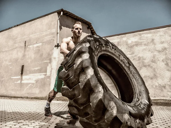 Handsome muscular young man exercising, flipping big tire outdoor