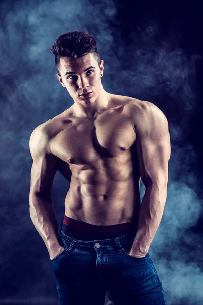ハンサムな若い筋肉男の上半身裸がスタジオ撮影で暗い背景にジーンズを着てください — ストック写真