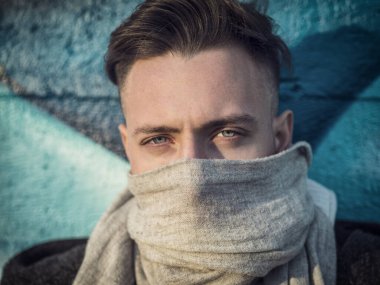 Boynunda atkısı olan bir adam, burnunu ve ağzını gizliyor..