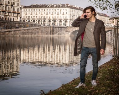 Nehrin kenarında cep telefonuyla konuşan bir adam. İtalya, Torino 'da, nehir kenarında telefonla konuşan bir adamın fotoğrafı.