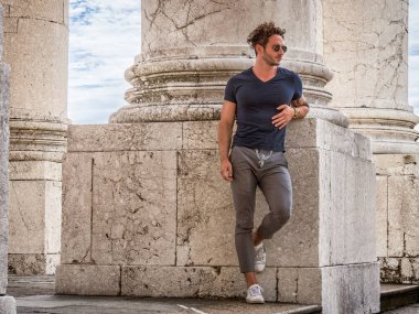 Mavi gömlekli ve gri pantolonlu bir adam bir sütuna yaslanıyor. Mavi gömlekli ve gri pantolonlu bir adamın sütuna yaslandığı fotoğraf.