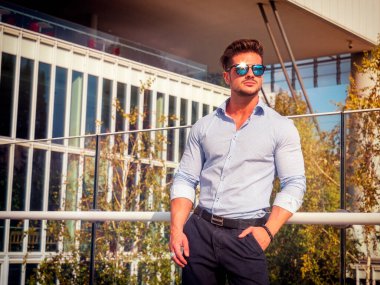 Binanın önünde duran güneş gözlüğü takan bir adam. Modern bir mimari başyapıtın önünde poz veren şık bir adamın fotoğrafı.