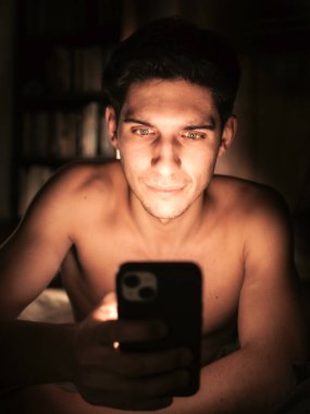 Üstsüz bir adam cep telefonuna bakıyor.