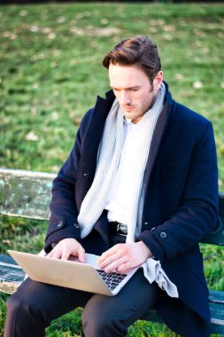 Dizüstü bilgisayarlı bir adam bankta oturuyor.