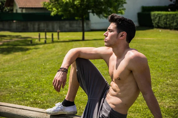 A shirtless man sitting on a bench in a park. Photo of a man enjoying a peaceful moment on a park bench