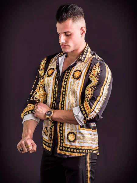 A man in a black and gold shirt and black pants. Photo of a stylish man in a black and gold outfit on dark background in studio